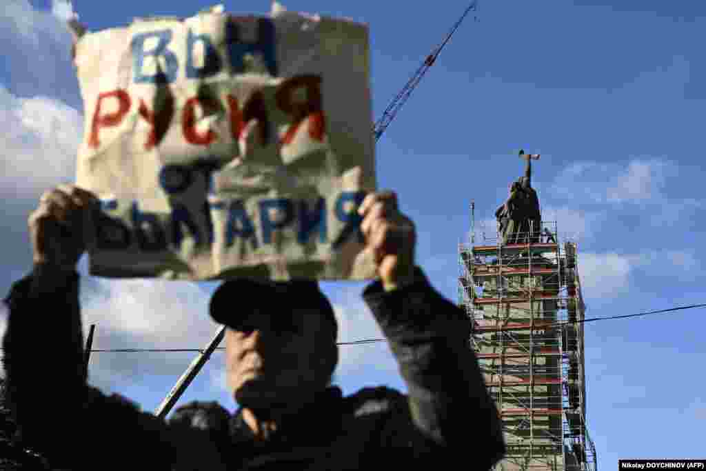 Мужчина держит плакат с надписью «Вон Россию из Болгарии», в то время как рабочие готовят леса вокруг памятника Советской армии перед его демонтажем в Софии.