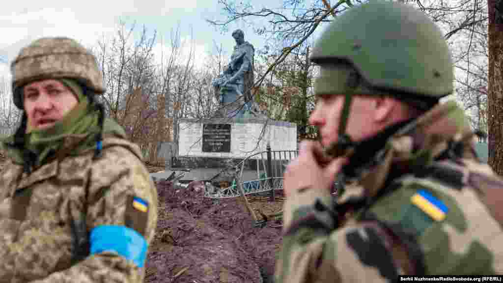 Украинские военнослужащие стоят возле поврежденного мемориала погибшим воинам во Второй мировой войне в недавно освобожденном селе Лукьяновка Киевской области, 27 марта 2022 года.