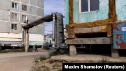 Мужчина идет мимо зданий, построенных на бетонных сваях в вечной мерзлоте