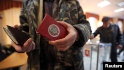 Un alegător în Crimeea își prezintă documentul de identitate purtând încă stema URSS-ului.
