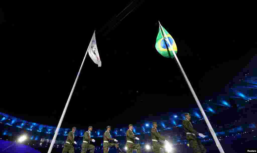 Brazilian soldiers march past the Olympic and Braziilian flags.