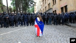 Un manifestant îmbrăcat în steagurile naționale georgiene și ale UE stă în fața unui cordon de poliție în timpul unui protest al opoziției la Tbilisi. 