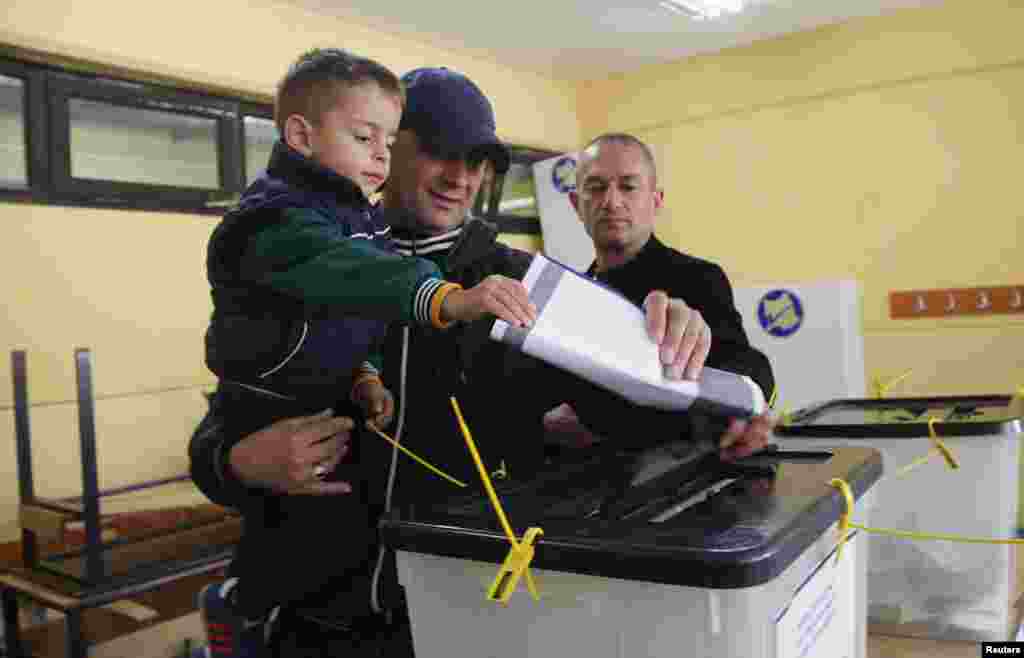 A Kosovar Albanian man and his son drop his ballot into a voting box at a polling station in the southern part of Mitrovica.