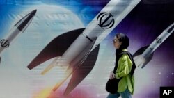 Жена преминава край плакат с ракети, носещи емблемата на Ислямска република Иран, Техеран
